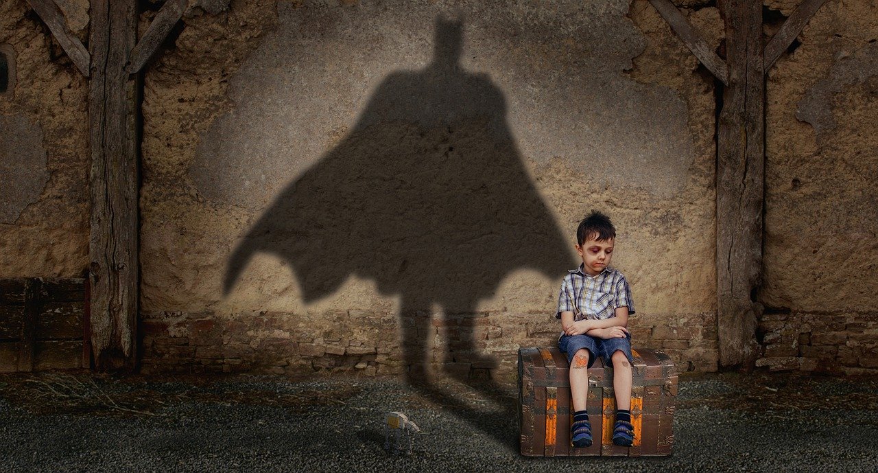 Junge sitzend wirft Schatten in Form von Batman